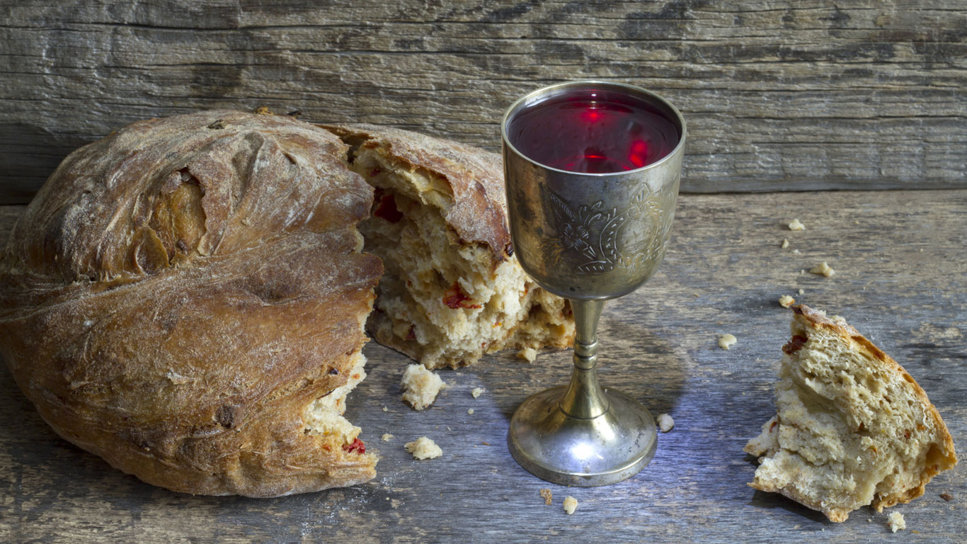 Silberner Kelch mit Wein neben einem Laib Brot